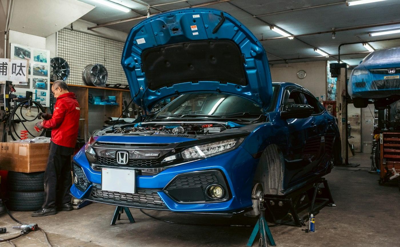 Technician working on a blue Honda with the bonnet open